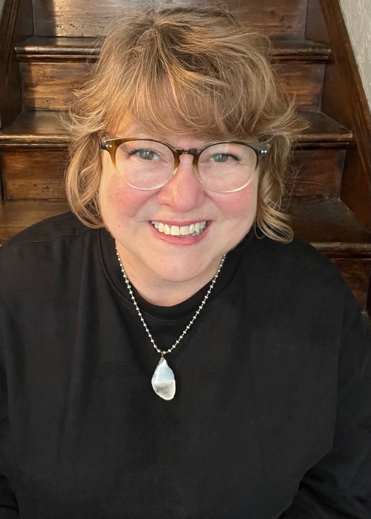 Photo of smiling woman wearing glasses, a black shirt, and a geode necklace that looks like it's laughing